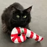 Schwarze Katze mit einer großen rot-weißen Zuckerstange aus Stoff